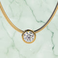 Gold necklace with a round diamond pendant on a beige background