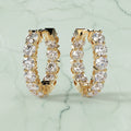 Gold hoop earrings with clear gemstones on a beige background