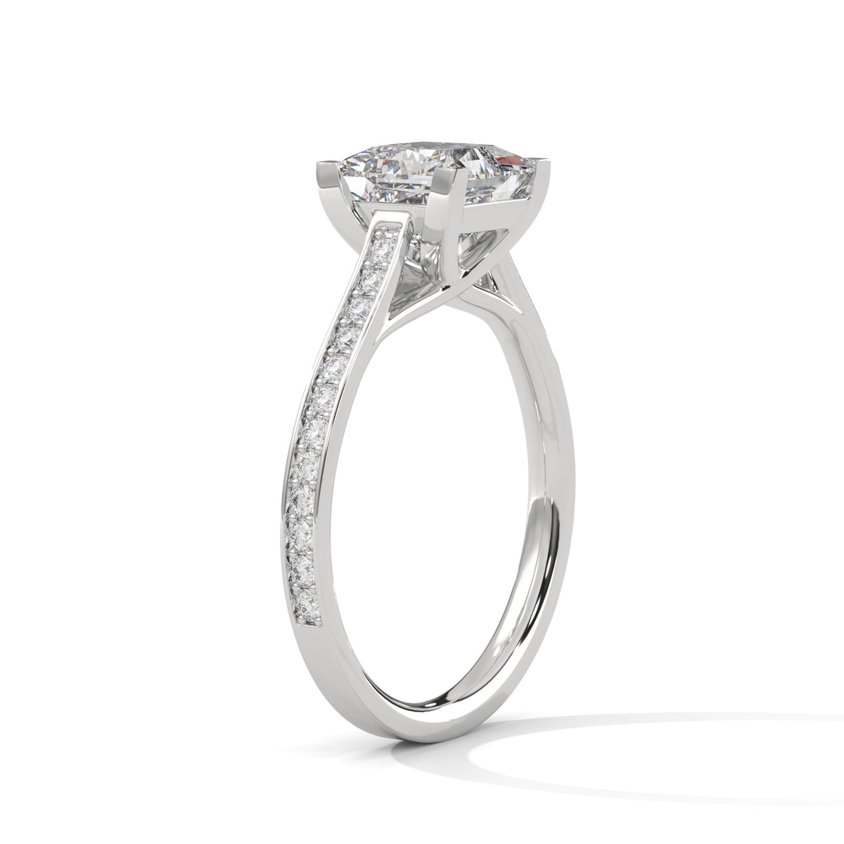 A silver-toned diamond engagement ring featuring a round brilliant-cut center stone in a four-prong setting, with a pavé band channel-set with smaller diamonds, shown on a clean white background.