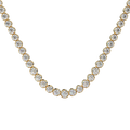 A gold tennis necklace featuring round-cut clear gemstones in a classic prong setting, displayed against a solid pale beige background.