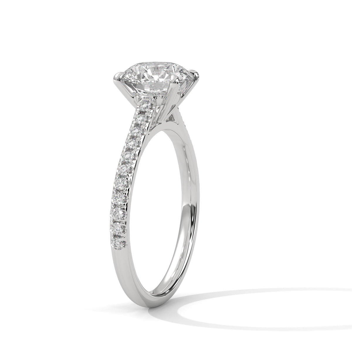 A silver-toned solitaire engagement ring with a round-cut diamond center stone and pavé-set diamonds along the shank, shown on a clean white background with a soft shadow.